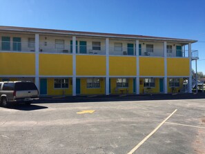 A two-story motel with a yellow facade, a parking lot, and a staircase leading to the upper level. - Economy Suites (Winter Haven)
