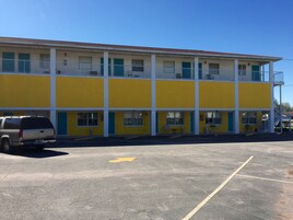 A two-story motel with a yellow facade, a parking lot, and a staircase leading to the upper level.
