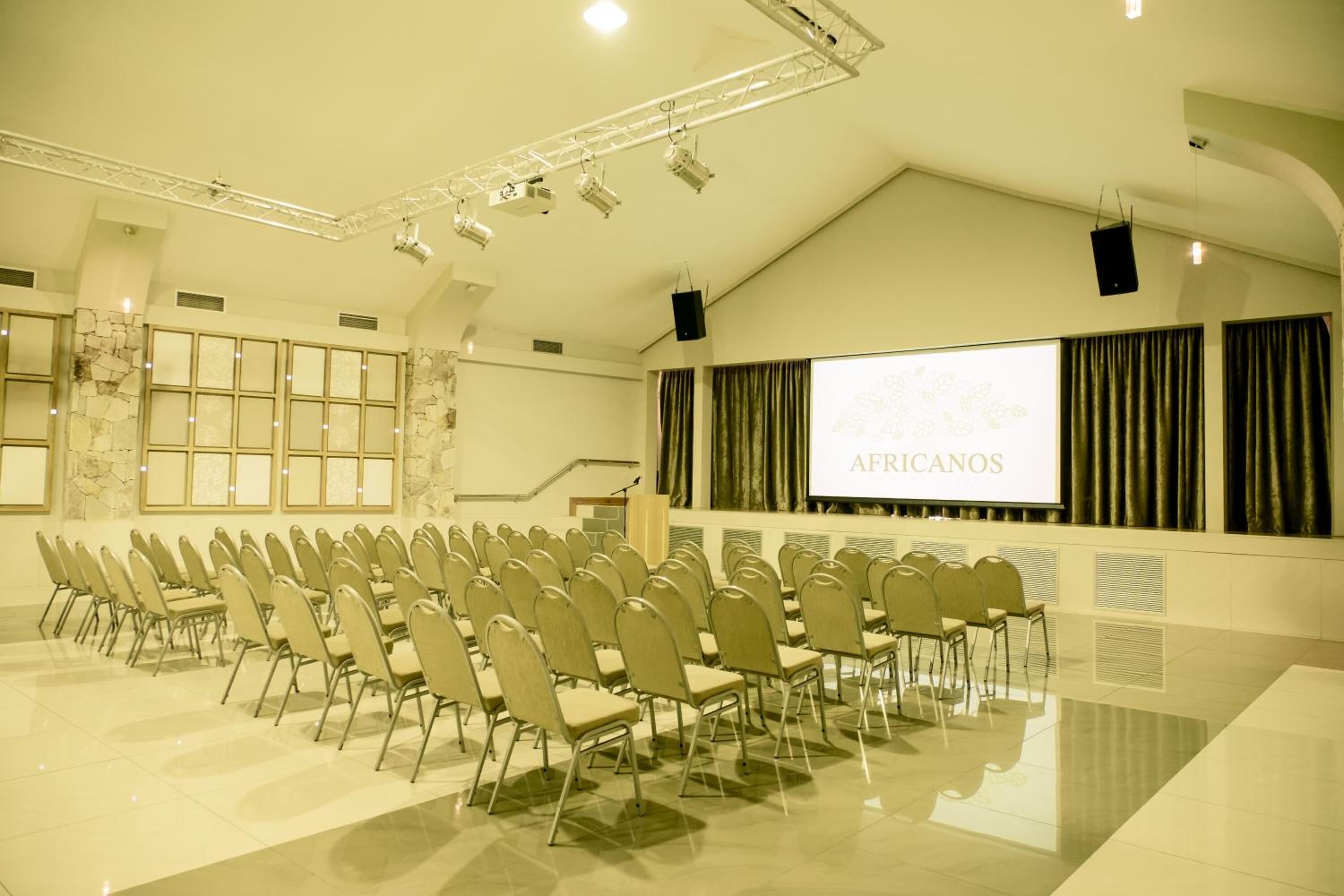 A conference room with rows of chairs, a projector screen displaying "AFRICANOS," and a stage with a podium.