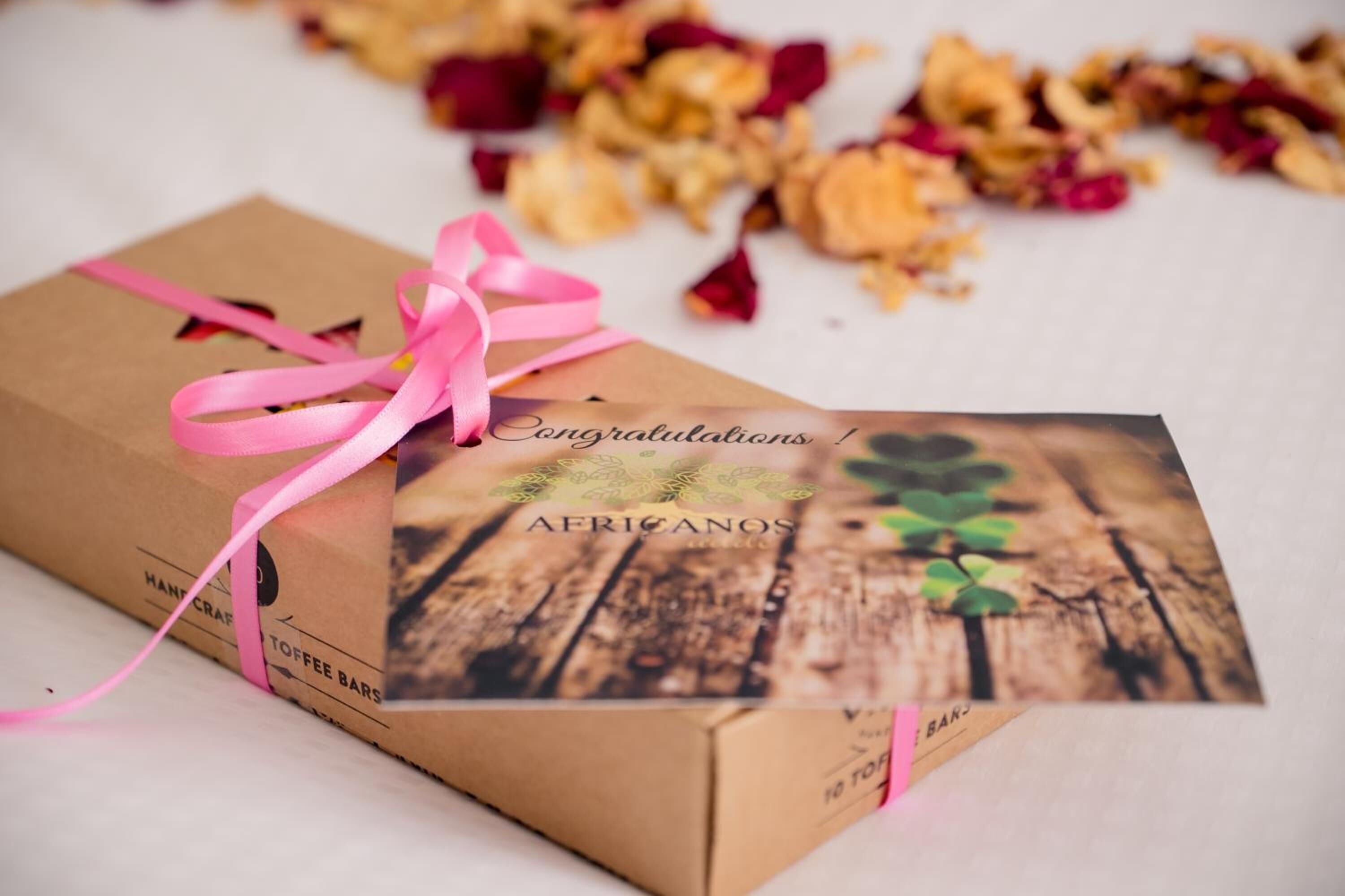 A brown gift box with a pink ribbon and a congratulatory card on top.