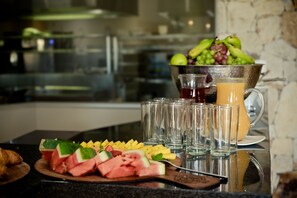 A breakfast setting with sliced fruits, a croissant, and a pitcher of juice on a kitchen counter.