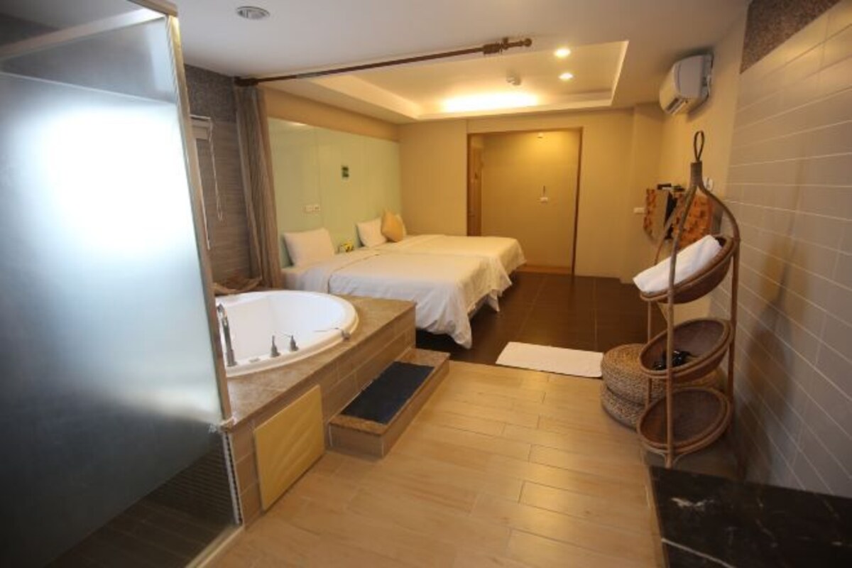 A hotel bathroom with a bathtub, two beds, a wooden bench, and a towel rack.