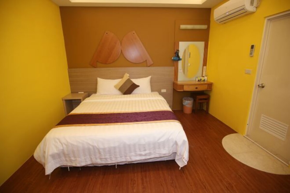 A hotel room with a bed, a nightstand, a mirror, and a door.