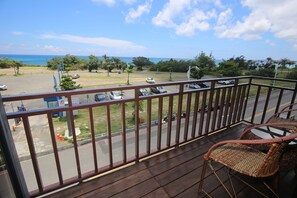 A wooden deck with wicker chairs overlooking a parking area and a view of the ocean. - Water Front Hotel (Hengchun)