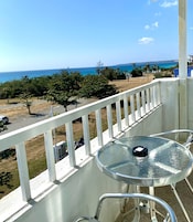 A balcony with a glass table and chairs, overlooking a beach with palm trees and a clear blue sky.