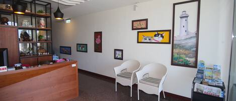 Un área de recepción con un escritorio de madera, dos sillas de mimbre y una pared decorada con obras de arte enmarcadas.
