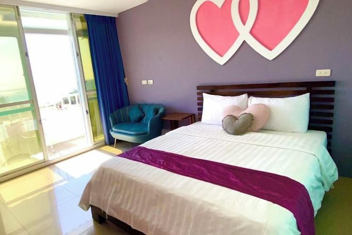 A bedroom with a bed, a nightstand, a blue chair, and a large window.