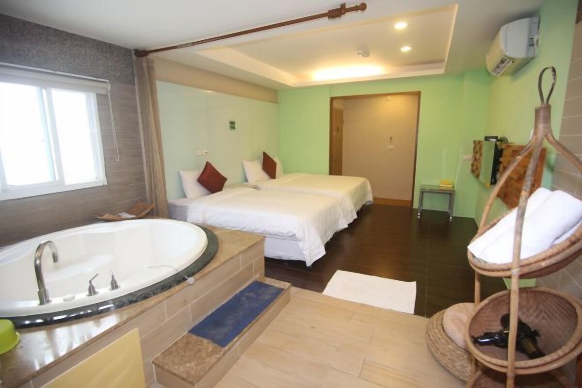 A hotel room with a large bathtub, two beds, a hanging chair, and a small table.