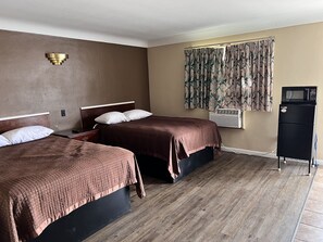 A hotel room with two beds, a wall-mounted air conditioner, a black refrigerator, and a window with patterned curtains. - Crown Inn (Toledo)