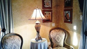 Ein Zimmer mit einer Lampe auf einem kleinen Tisch, zwei gemusterten Stühlen und gerahmten Kunstwerken an der Wand.