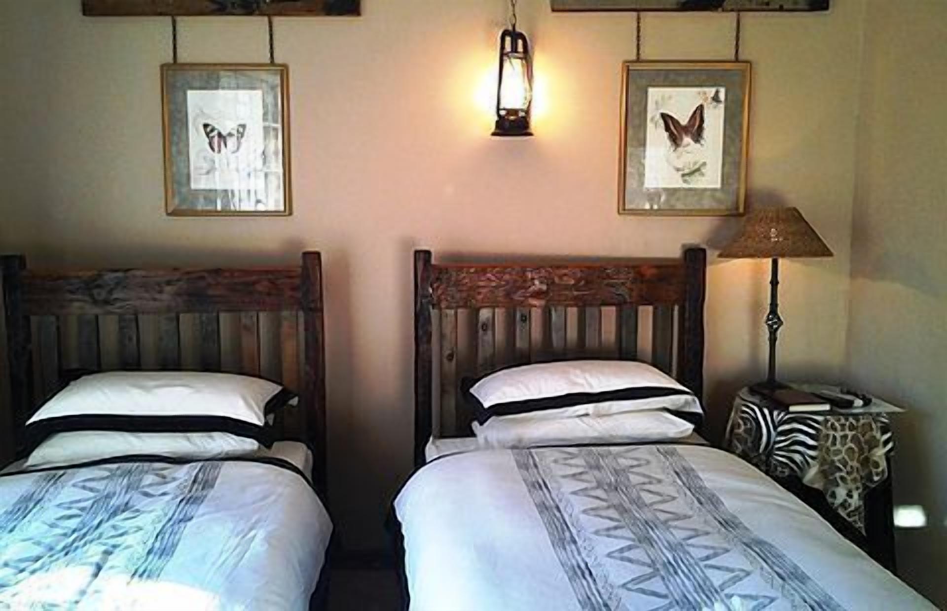 Deux lits avec des têtes de lit en bois, une table de chevet avec une lampe et des tableaux représentant des papillons, accrochés au mur.