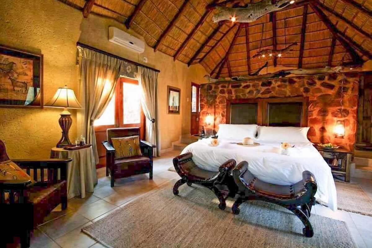 Une chambre spacieuse avec un grand lit, un mur en pierre, un toit de chaume et une chaise en bois rustique.