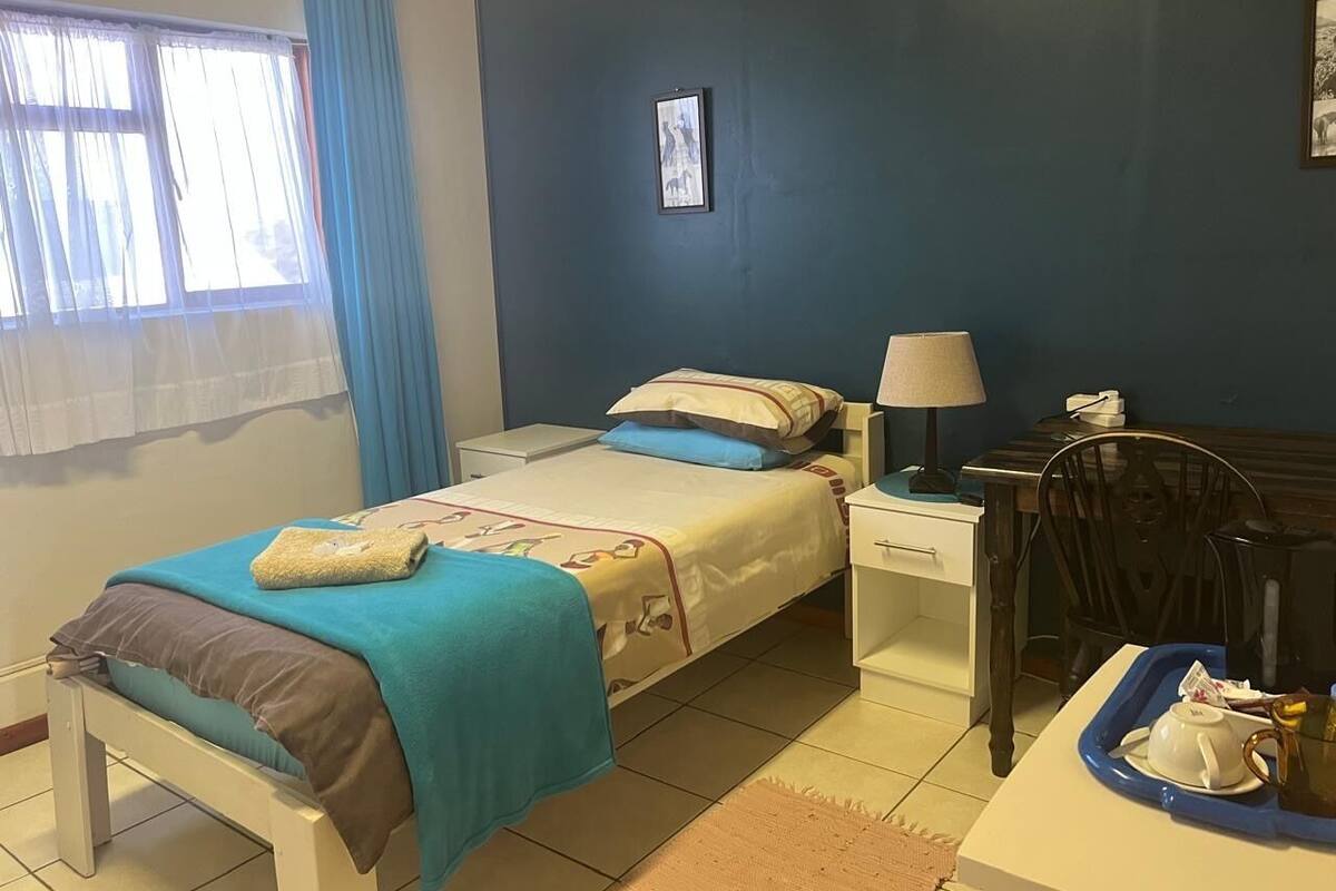 A bedroom with a bed, bedside table, chair, and a small table with a tray.