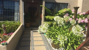 A pathway leading to a building entrance with a decorative door, surrounded by various plants and flowers.
