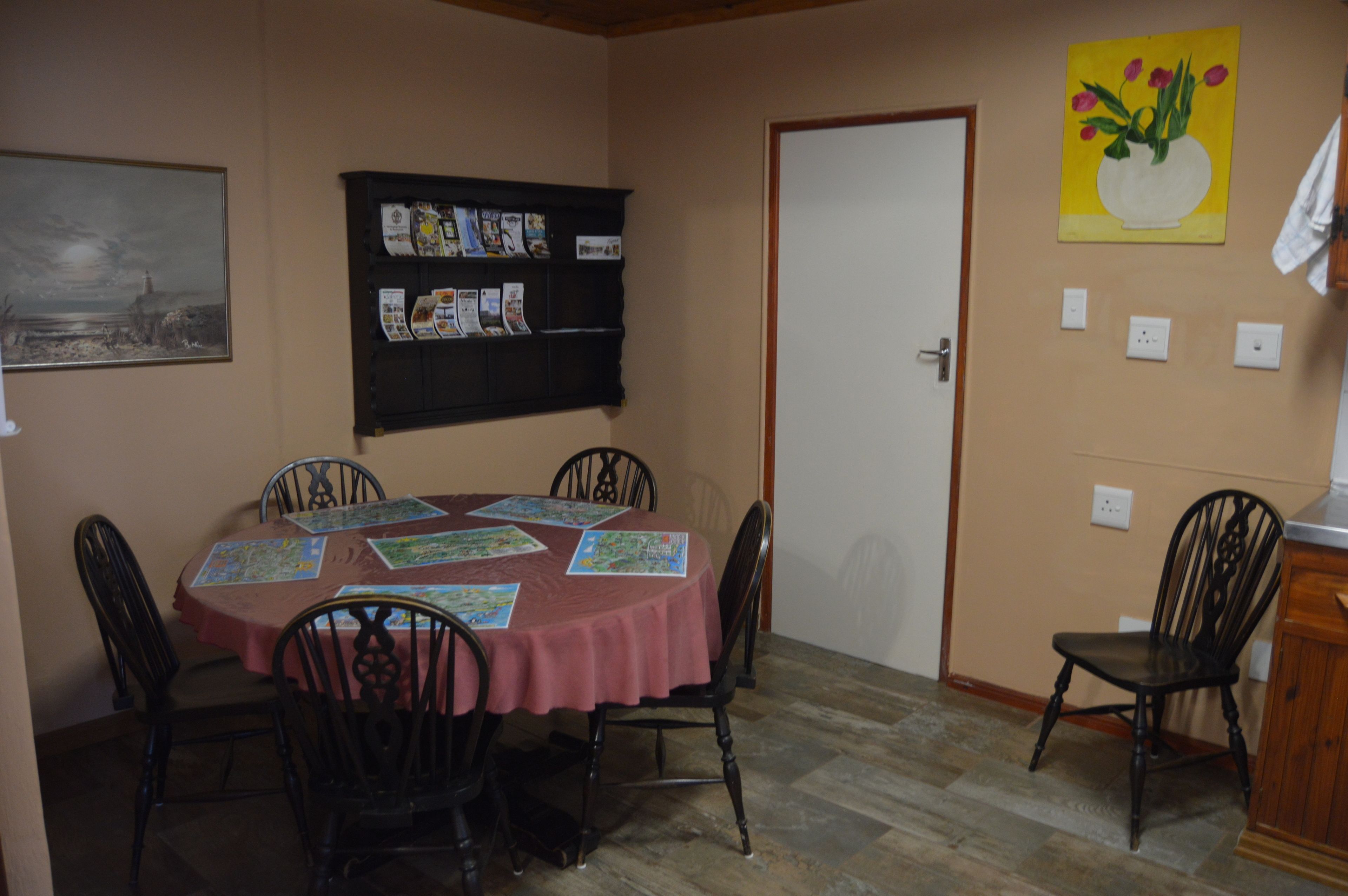 A dining area with a table set for four, surrounded by chairs, a bulletin board with various papers, and a door with a light switch.
