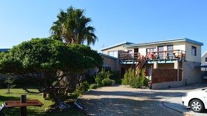 A building with a covered outdoor area, a gravel driveway, and a parked car. - Fisherhaven Traveller's Lodge - Hostel (Hermanus)