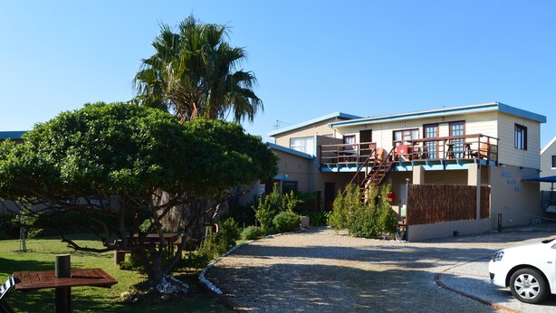 A building with a covered outdoor area, a gravel driveway, and a parked car.