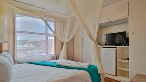 A hotel room with a bed, a TV, a refrigerator, and a window with curtains.