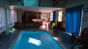 An indoor swimming pool with a tiled floor, surrounded by wooden chairs and a table.