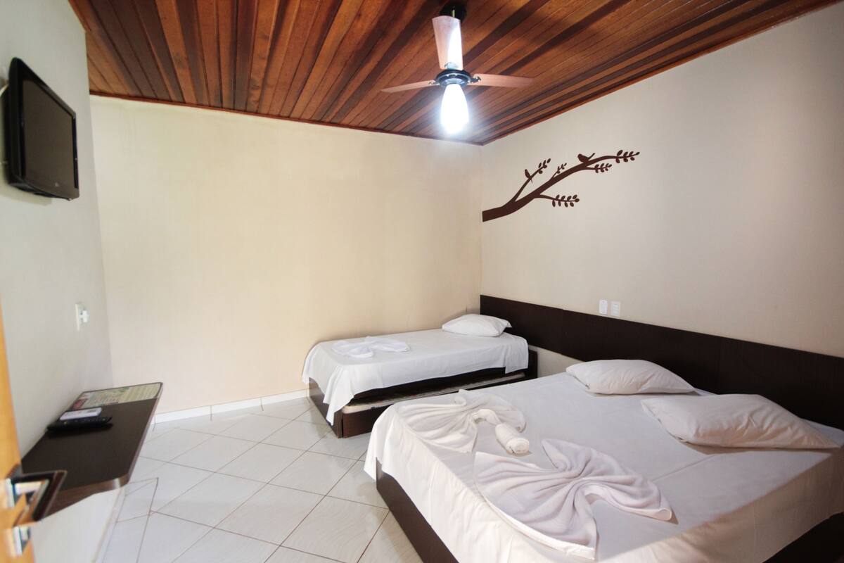 Une chambre d’hôtel avec deux lits, un ventilateur de plafond, un téléviseur fixé au mur et un sol carrelé.