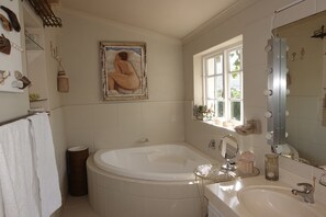 A bathroom with a bathtub, a sink, a vanity mirror, and a window with a view of greenery.
