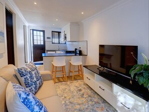 A modern living room with a sofa, a TV, and a kitchen area with a bar. - Cloverleigh Guest House (Wilderness)