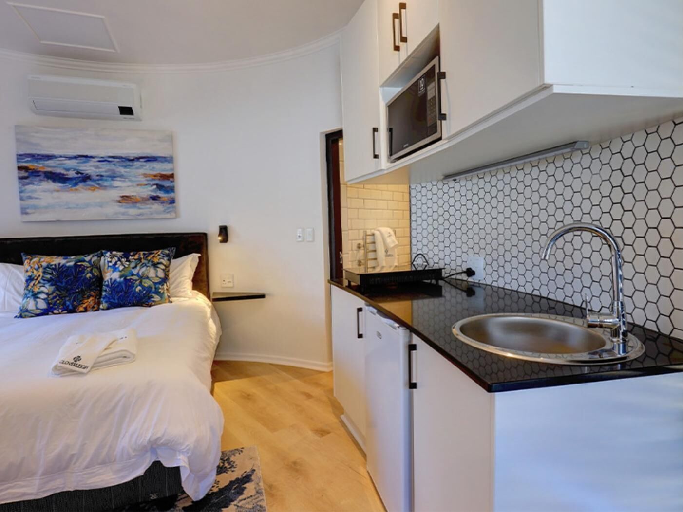 Una habitación de hotel compacta con cama, una kitchenette pequeña y un cuadro en la pared.