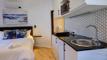 Una habitación de hotel compacta con cama, una kitchenette pequeña y un cuadro en la pared.