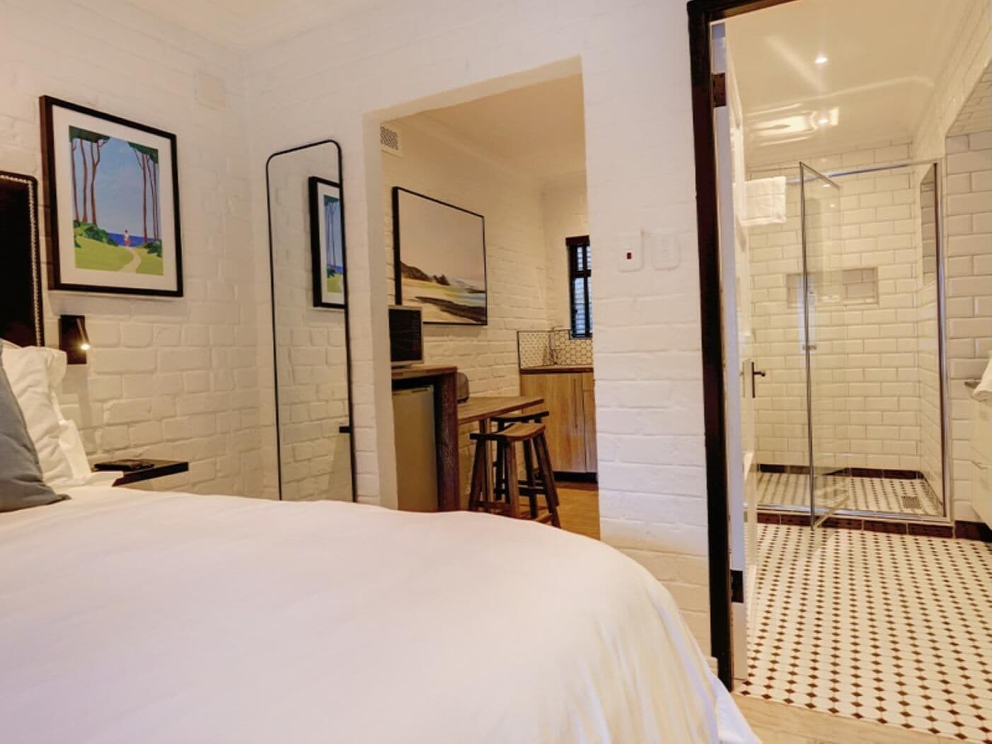 Una habitación de hotel con una cama grande, un escritorio, una silla y una zona de ducha con paredes de vidrio.