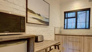 A kitchen with a microwave, toaster, and wooden table with a stool. - Cloverleigh Guest House (Wilderness)