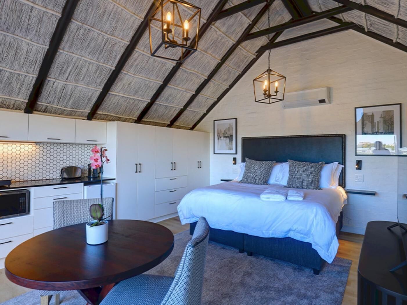 A bedroom with a large bed, a dining table with chairs, and a kitchen area with cabinets and a countertop.