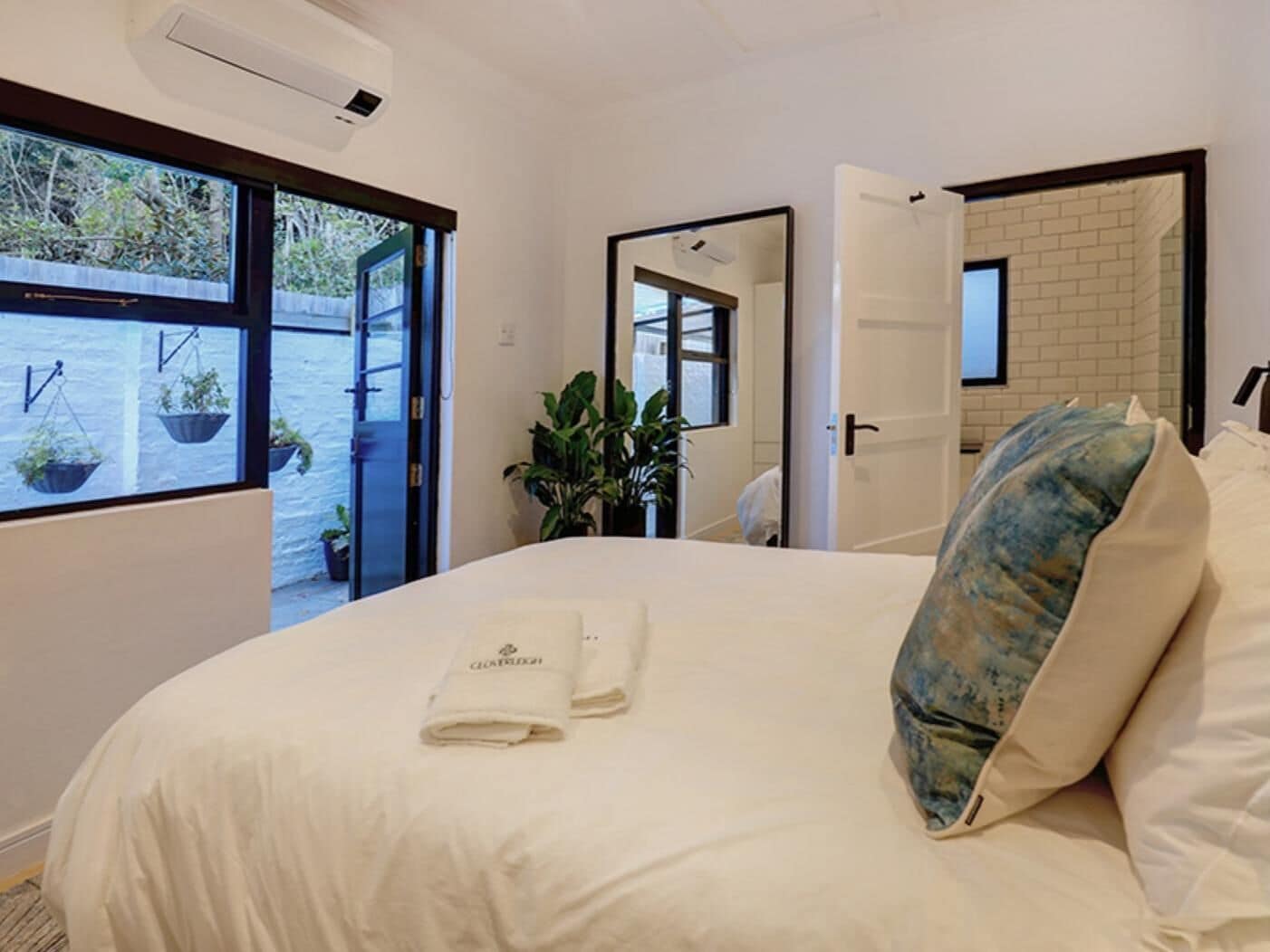Una habitación de hotel con cama, ventana con vistas, espejo y puerta que da a otra habitación.