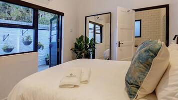 Una habitación de hotel con cama, ventana con vistas, espejo y puerta que da a otra habitación.