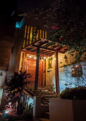 Une entrée moderne, agrémentée d’une pergola en bois, d’un espace salon extérieur et d’un mur en pierre sur lequel est fixée une enseigne.