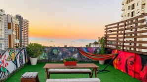 Une terrasse sur le toit avec une table et un banc en bois, un hamac et une fresque murale.