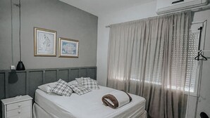Une chambre à coucher comprenant un lit, un ventilateur de plafond, une table de chevet, une commode et une fenêtre avec des rideaux.