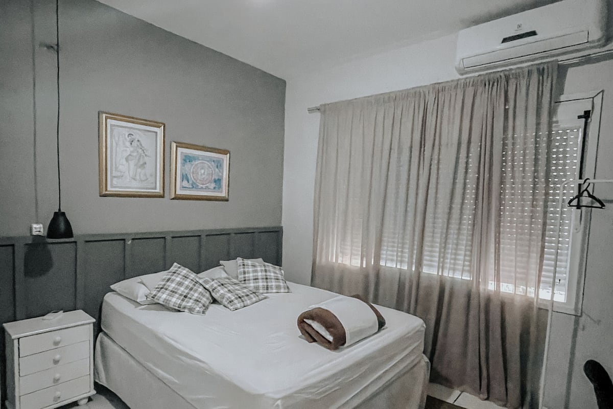 A bedroom with a bed, a ceiling fan, a nightstand, a dresser, and a window with curtains.