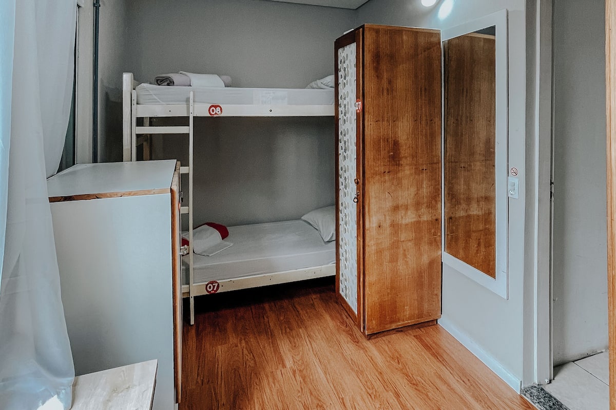 A compact room with a bunk bed, a wooden wardrobe, and a small desk.