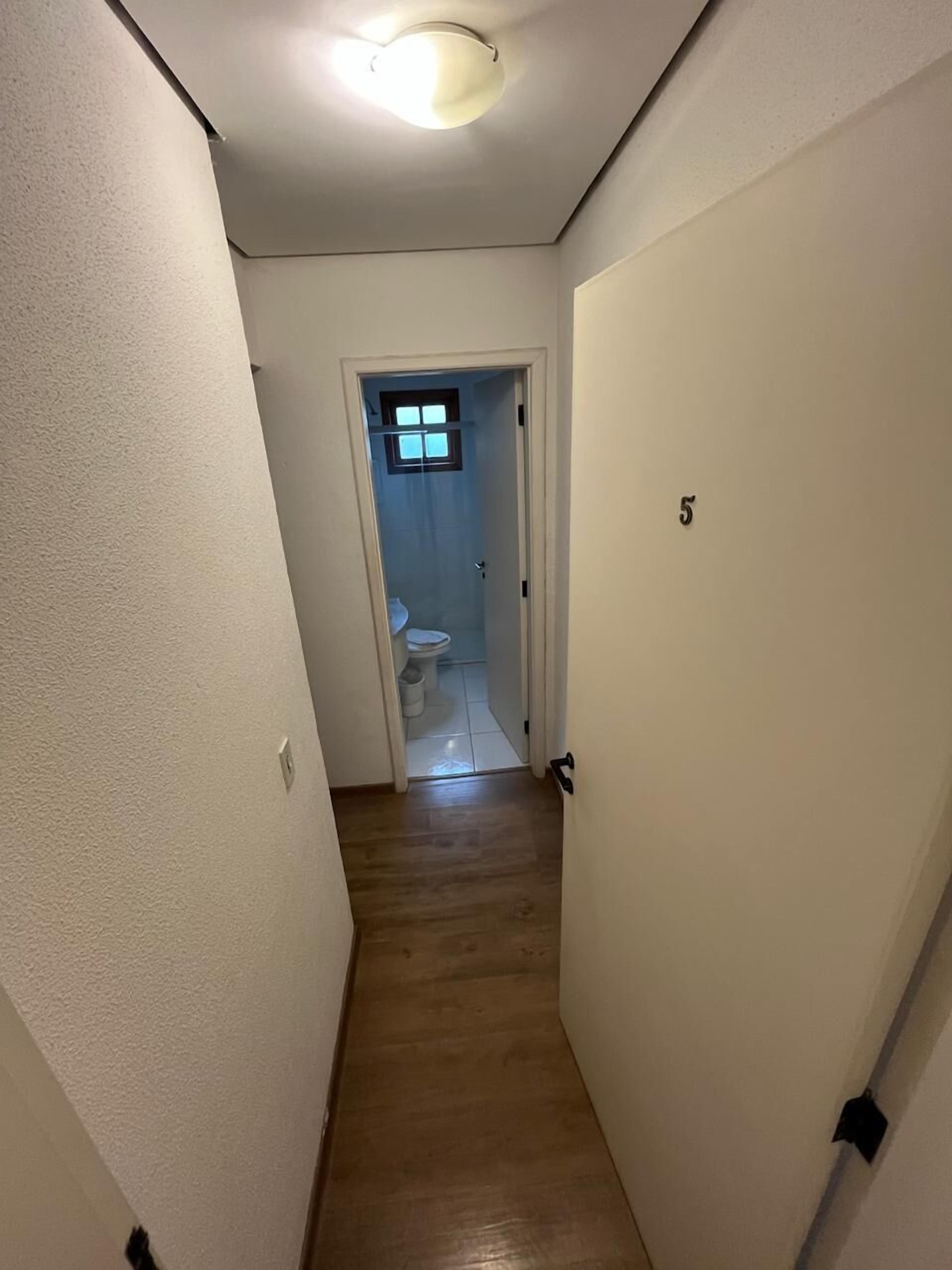 Un pasillo estrecho con piso de madera que lleva a un baño con inodoro y una ventana pequeña.