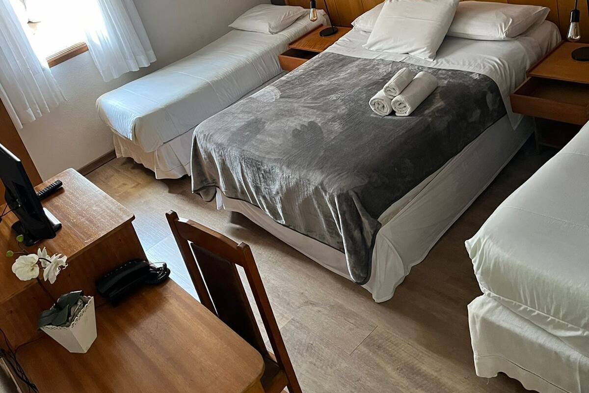 Una habitación de hotel con una cama grande, dos camas más pequeñas, un escritorio de madera y una silla.