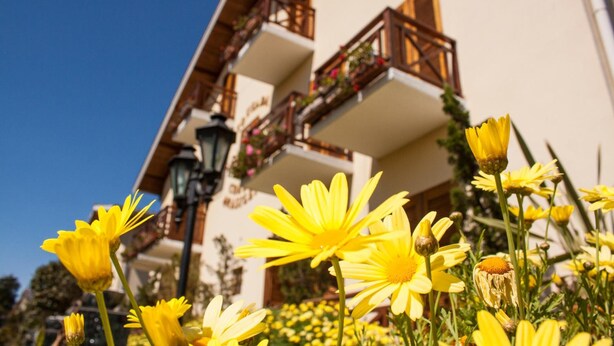 A building with balconies adorned with flowers and a clear blue sky. - Pousada Condado Brasileiro (Campos do Jordão)