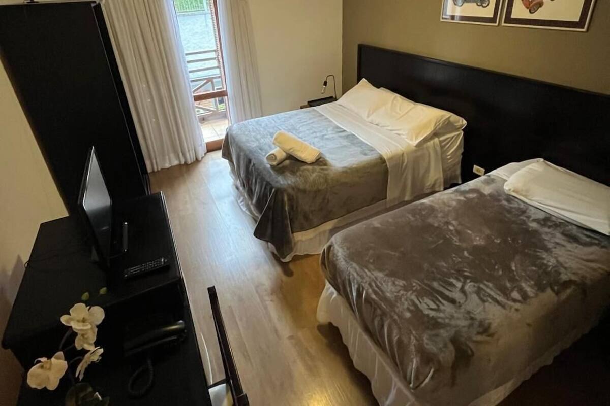 Habitación de hotel con dos camas, un escritorio con televisión y una ventana con cortinas.