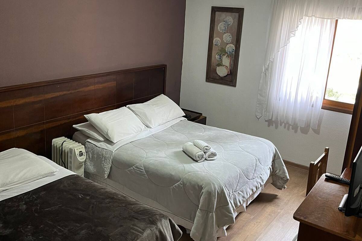 Habitación de hotel con dos camas, un escritorio, un radiador y una ventana con cortinas.