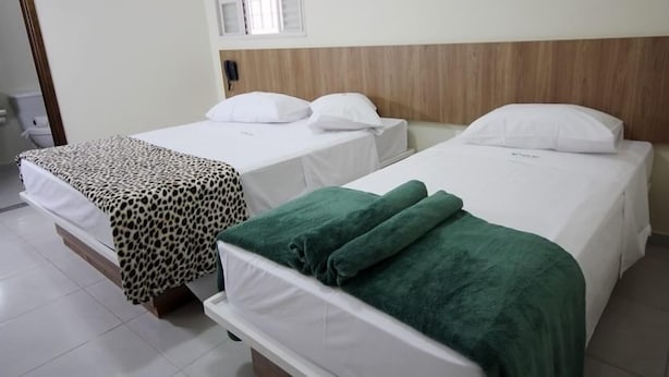 Ein Hotelzimmer mit zwei Betten, jedes mit einer weißen Matratze und passenden Kissen. Das Bett rechts hat ein Holz-Kopfteil, das Bett links eine Bettdecke mit Leopardenmuster.