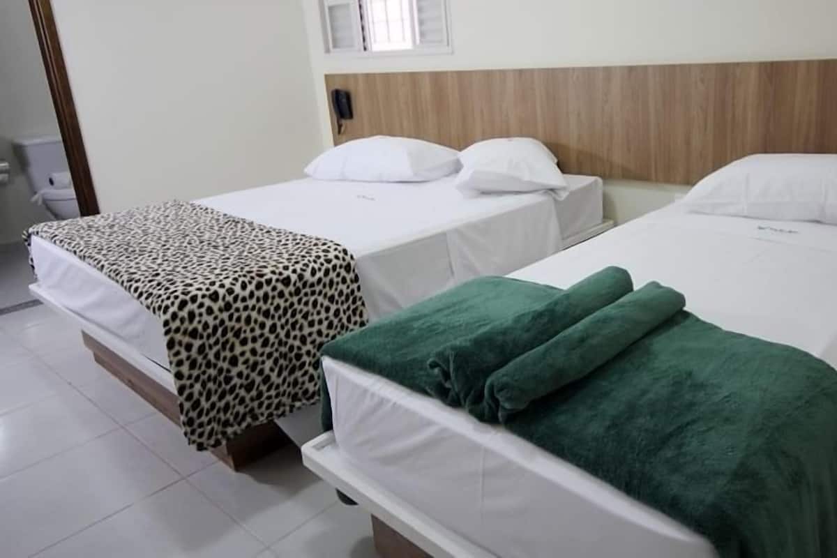 A hotel room with two beds, each with a white mattress and matching pillows. There is a wooden headboard on the right bed, and a leopard print cover on the left bed.