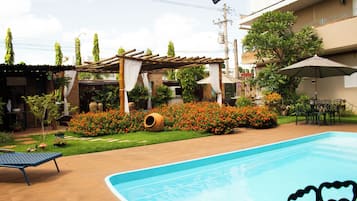 A swimming pool with a heart-shaped decoration, surrounded by a garden with various plants and a pergola structure.