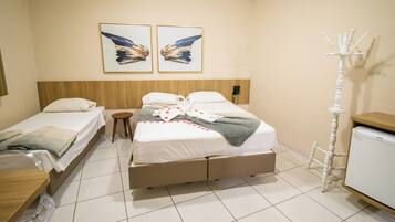 Een hotelkamer met een tweepersoonsbed, een enkele bed, een houten hoofdbord, een nachtkastje, een klein krukje, een kapstok en een koelkast.
