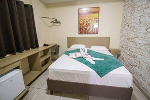 Quarto de hotel com cama, escrivaninha, cadeira, mini-frigorífico e parede de tijolos.