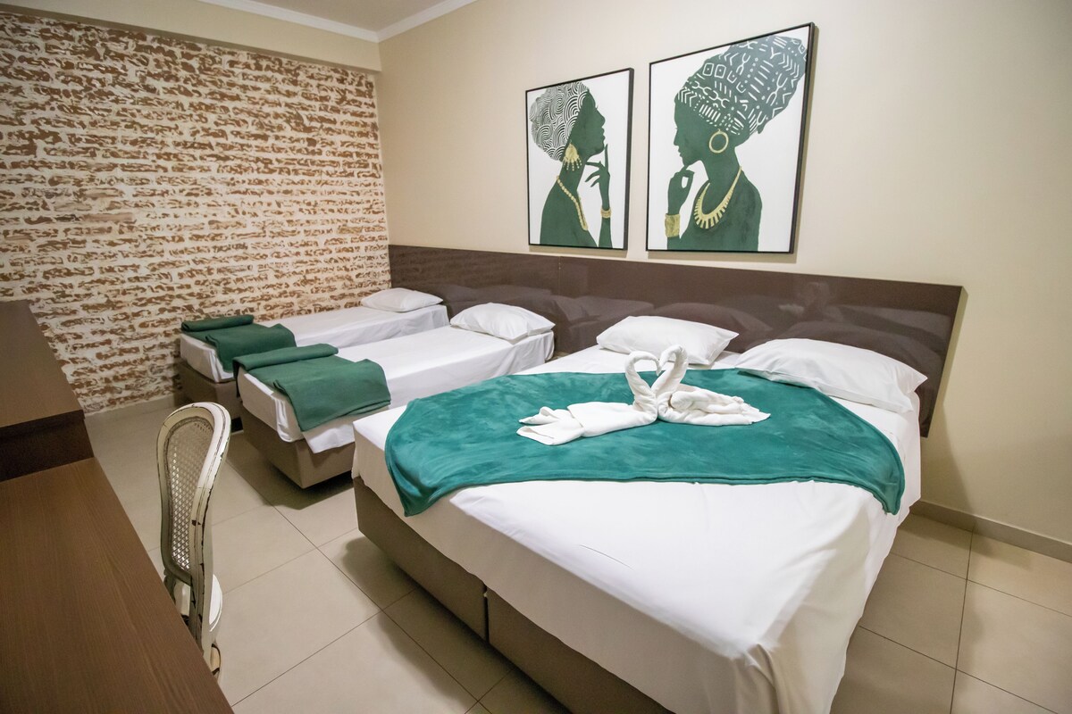 Quarto de hotel com duas camas, parede com padrão de tijolos e dois quadros emoldurados.