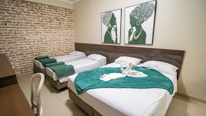 A hotel room with two single beds, a large bed with a green blanket, and a chair. There are two wall art pieces above the large bed.